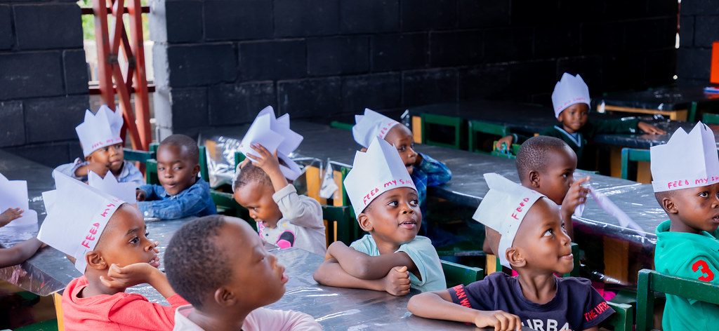 Children wearing paper chef hats at their tables during a meal day