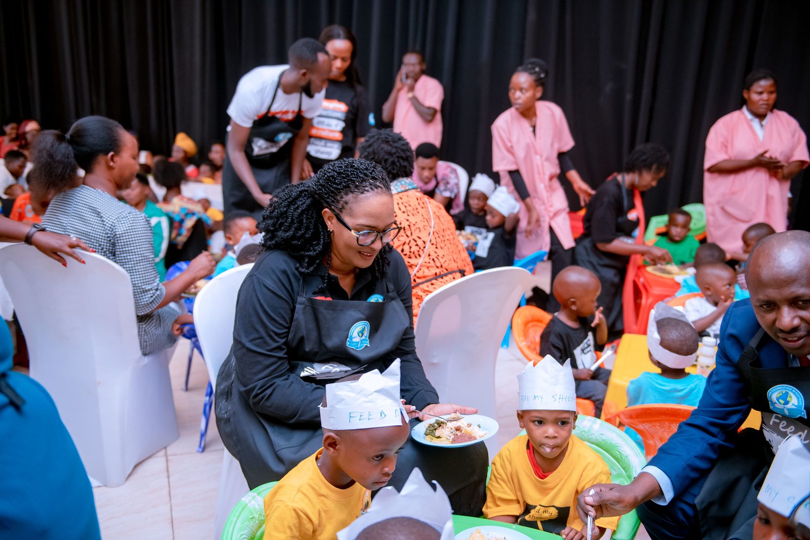 Children wearing paper crowns, eating lunch with caregivers on meal day